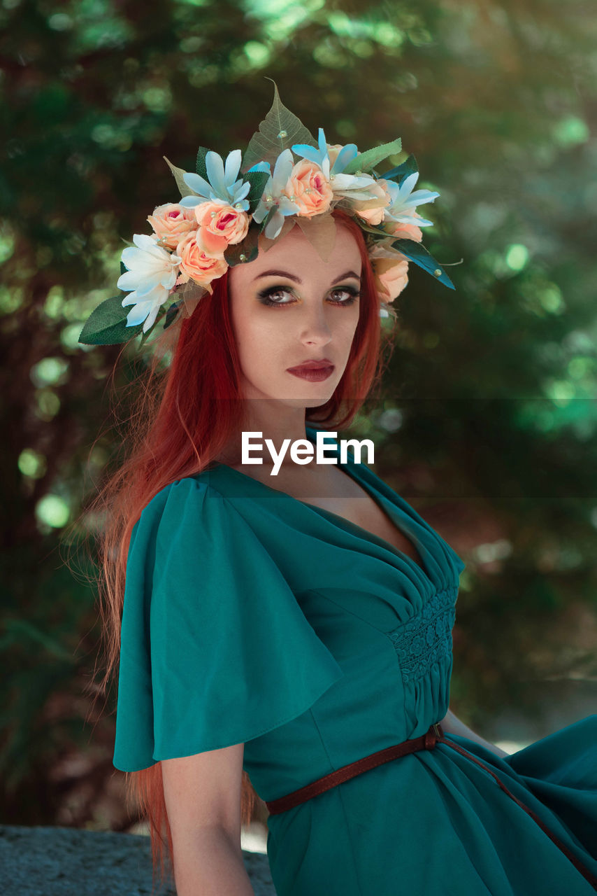 Portrait of beautiful woman wearing flowers while standing against trees