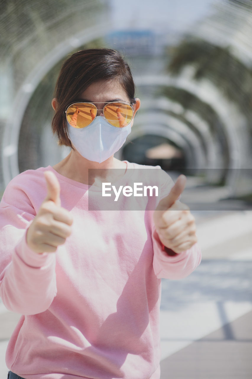 Portrait of woman with sunglasses gesturing while standing outdoors