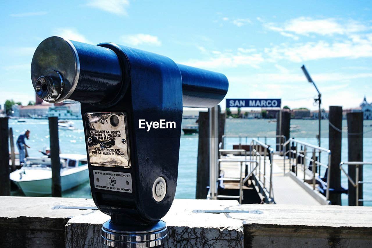 Close-up of coin-operated binoculars at harbor against sky