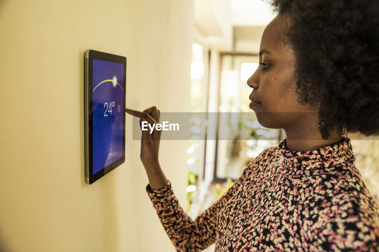 Afro woman using home automation device on wall