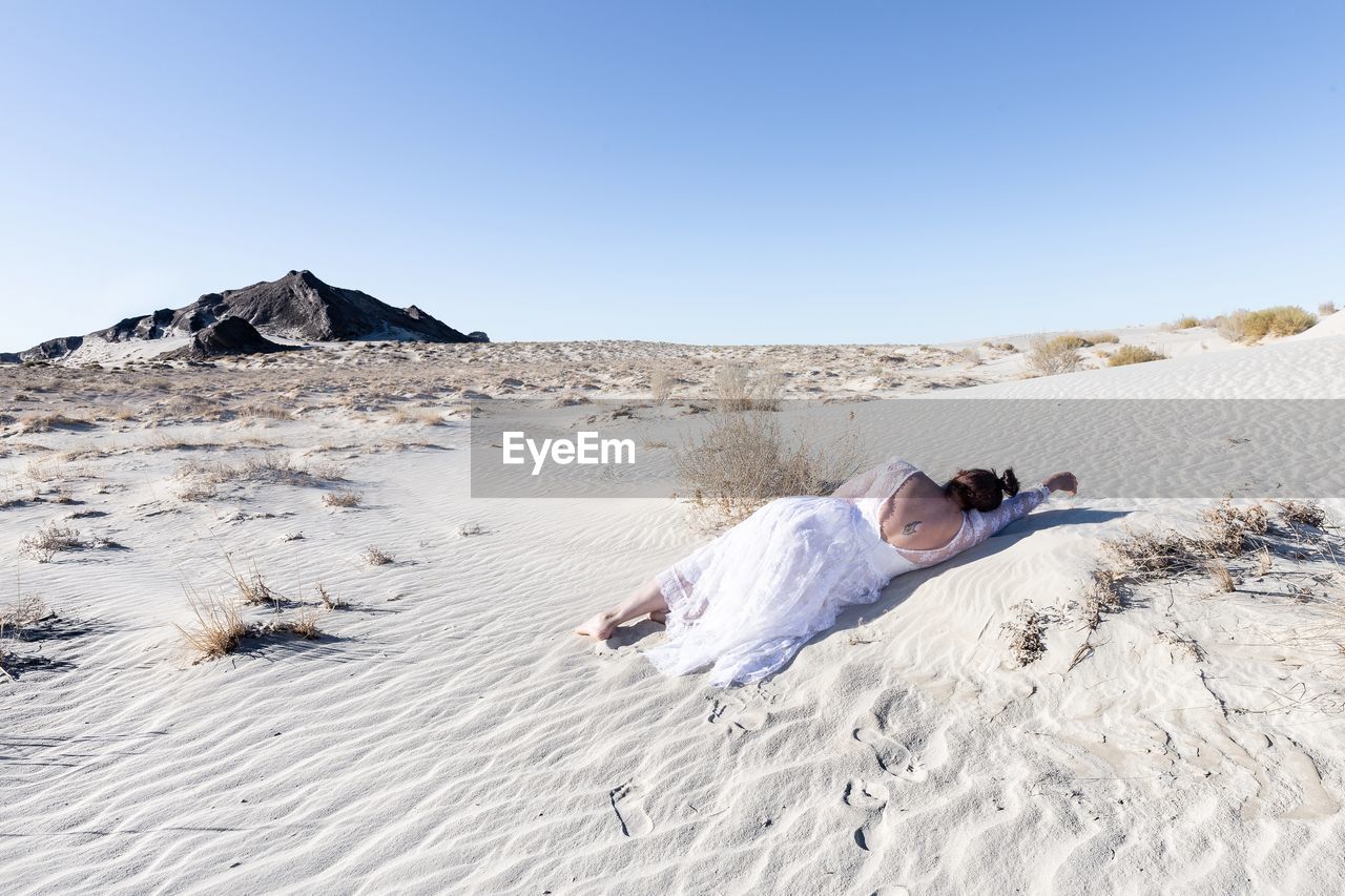 Woman lying on sand at desert against clear sky