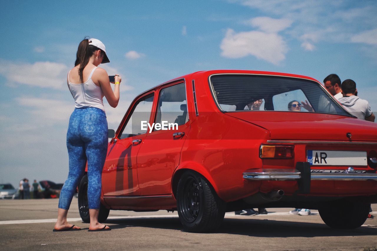 WOMAN STANDING ON CAR AGAINST SKY