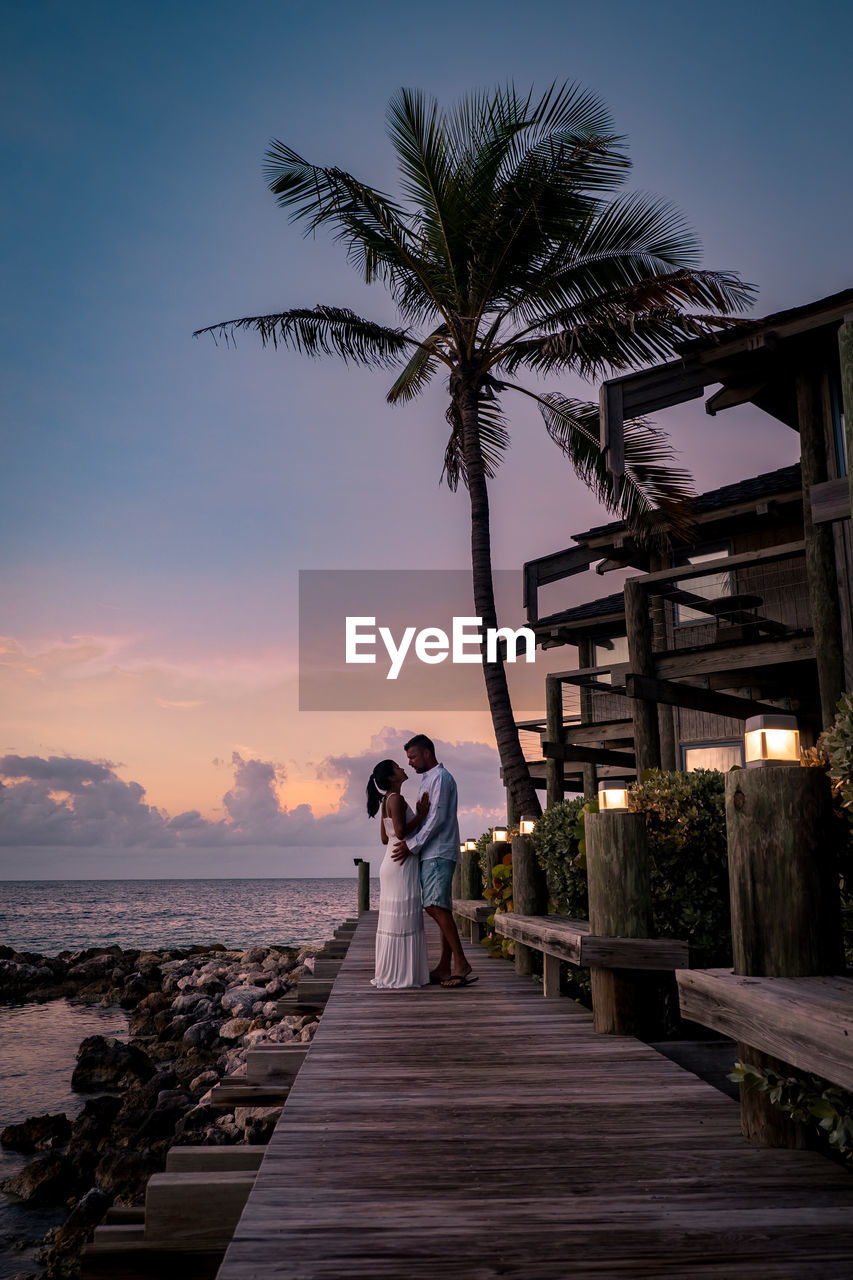 COUPLE WALKING BY PALM TREE AGAINST SEA