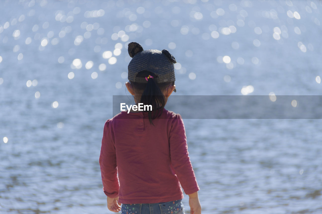 Rear view of girl standing against sea at beach