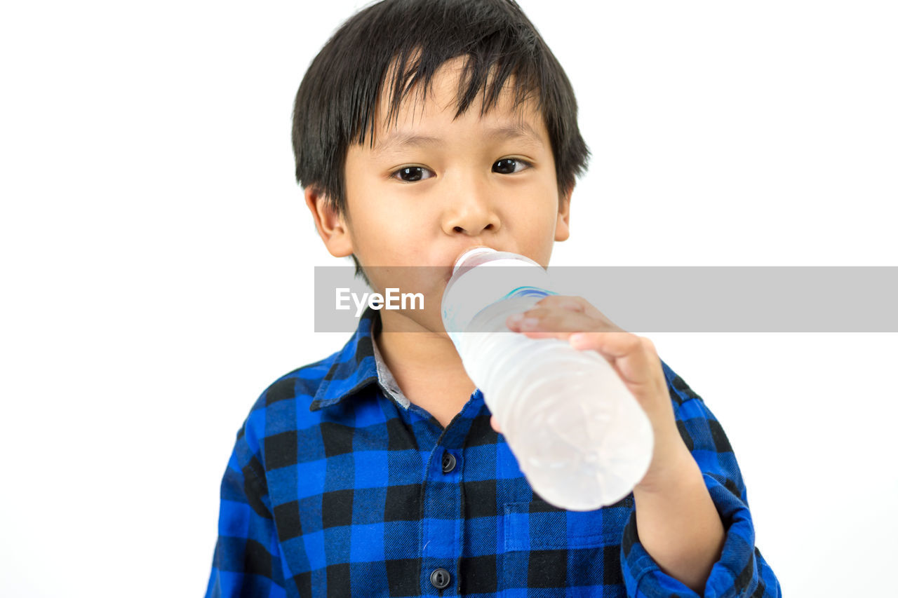 Portrait of boy drinking water from bottle against white background