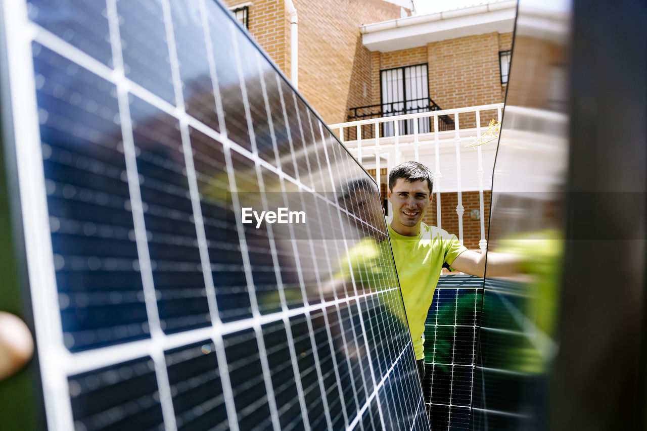 Happy engineer standing behind solar panel on sunny day