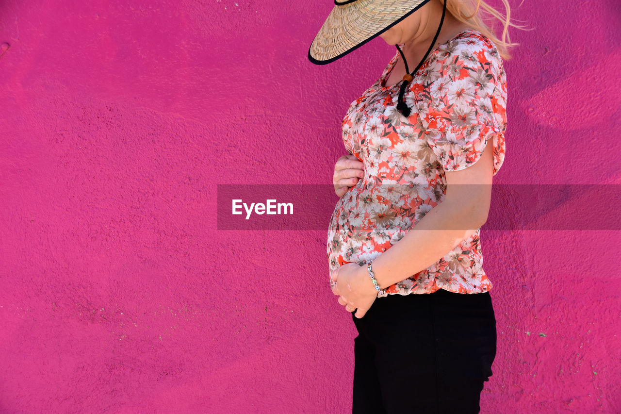 Pregnant woman standing by pink wall