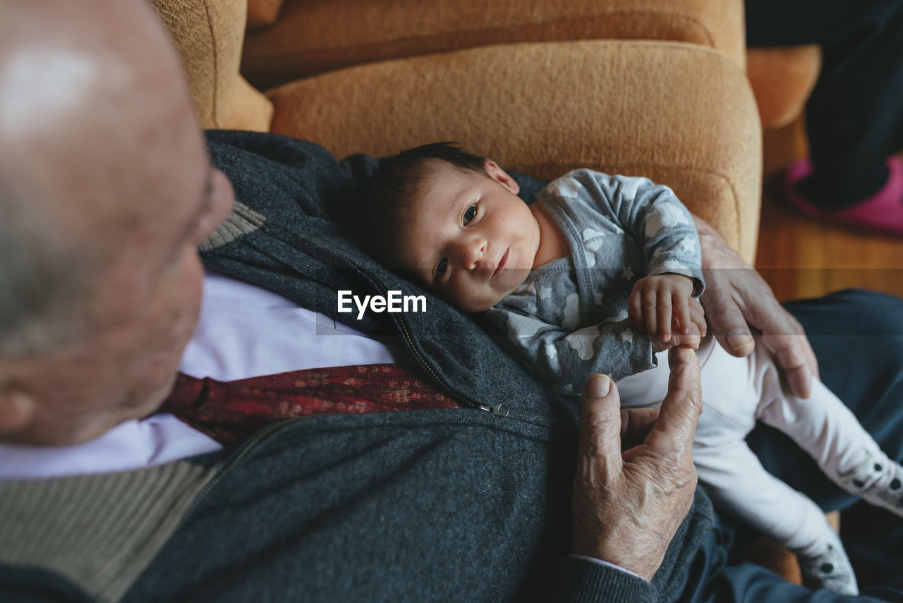 Newborn baby girl on the lap of great grandfather at home