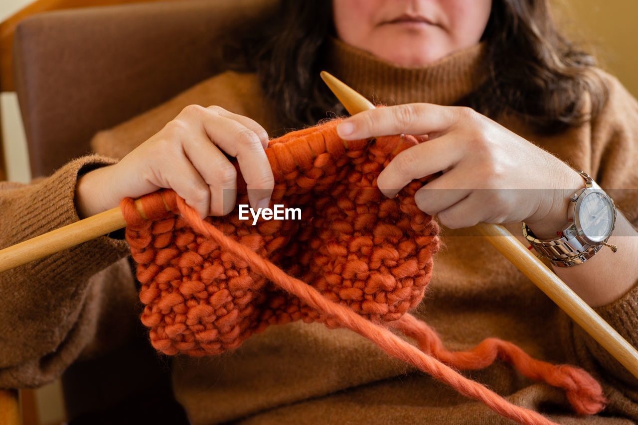 Woman knitting a cozy woolen garment sitting on her furniture at home. work at home concept.