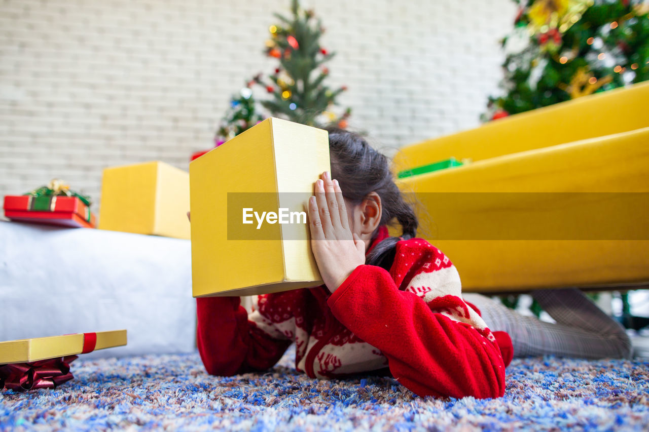 Close-up of girl holding christmas present while lying on rug