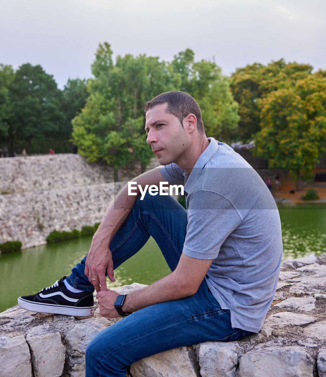 one person, adult, sitting, men, water, casual clothing, nature, leisure activity, rock, lifestyles, side view, relaxation, tree, plant, young adult, day, looking, contemplation, full length, vacation, outdoors, person, looking away, river, jeans, clothing, three quarter length, sky, footwear, beard, facial hair, tranquility, activity