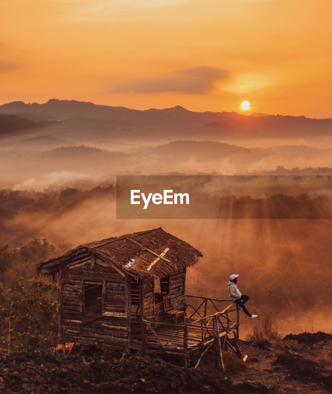 Man by hut against sky during sunrise