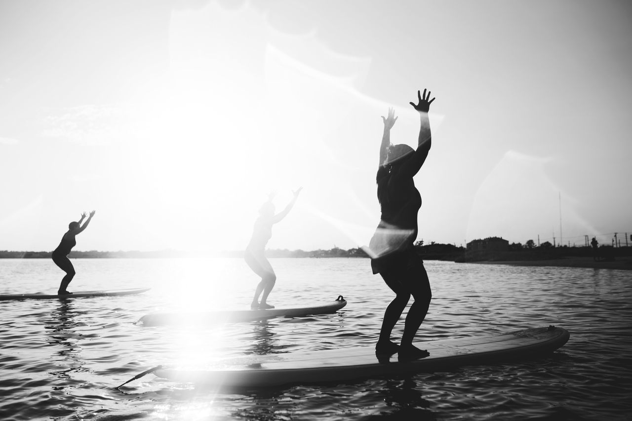 Silhouette people exercising on paddleboard in sea against sky