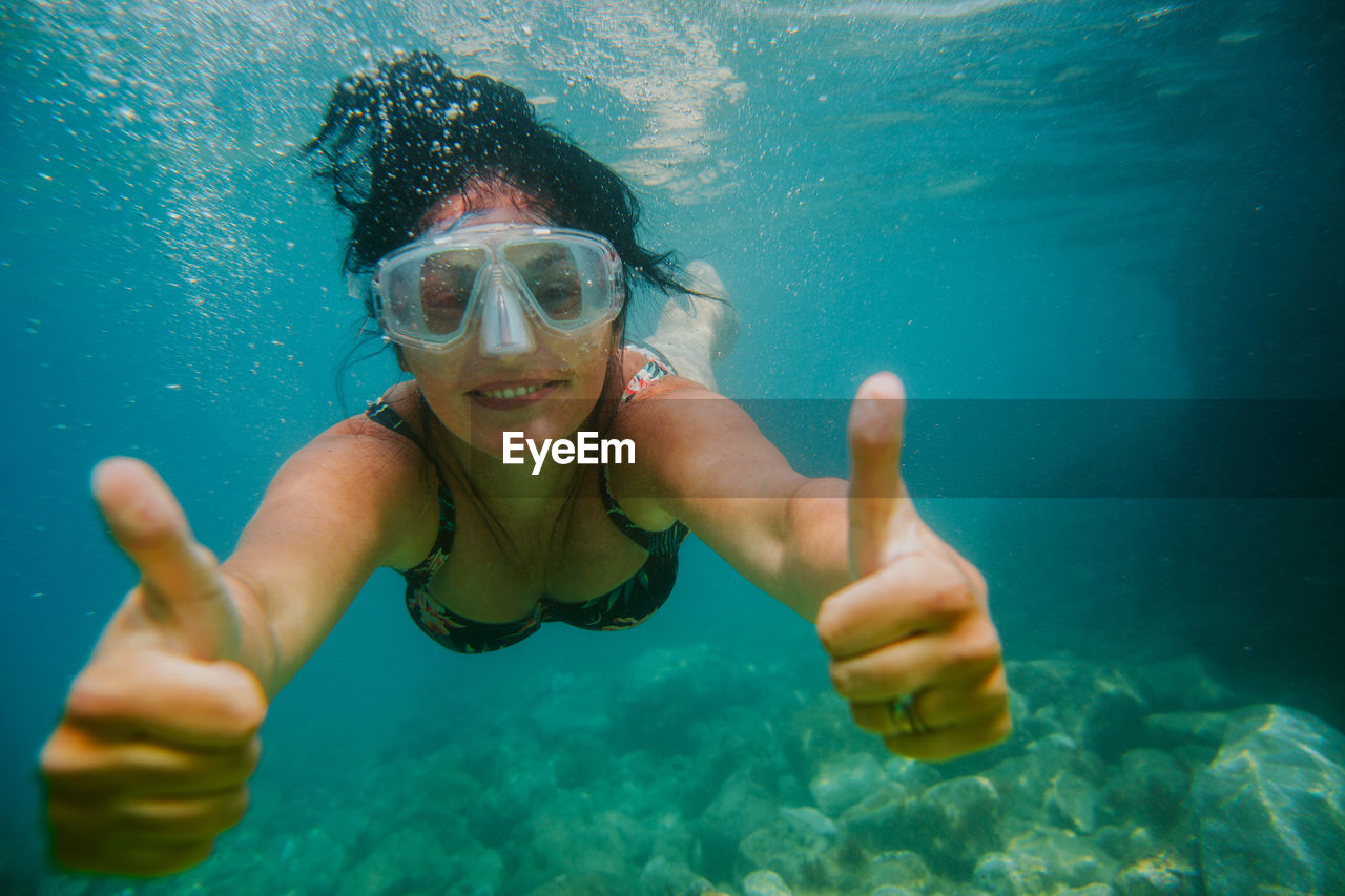 Portrait of woman swimming while gesturing thumbs up sign in sea