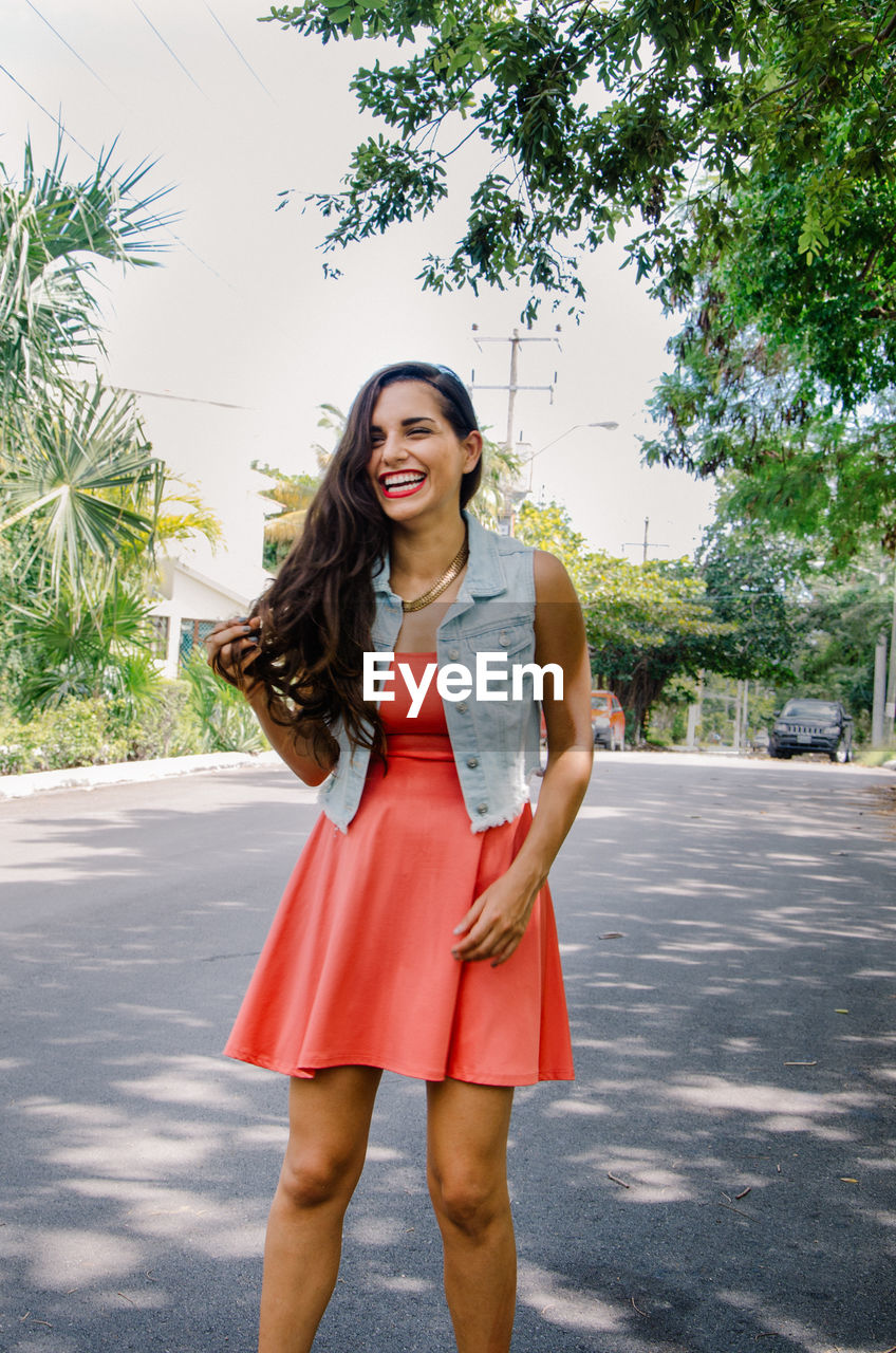 Happy beautiful woman standing on road against sky