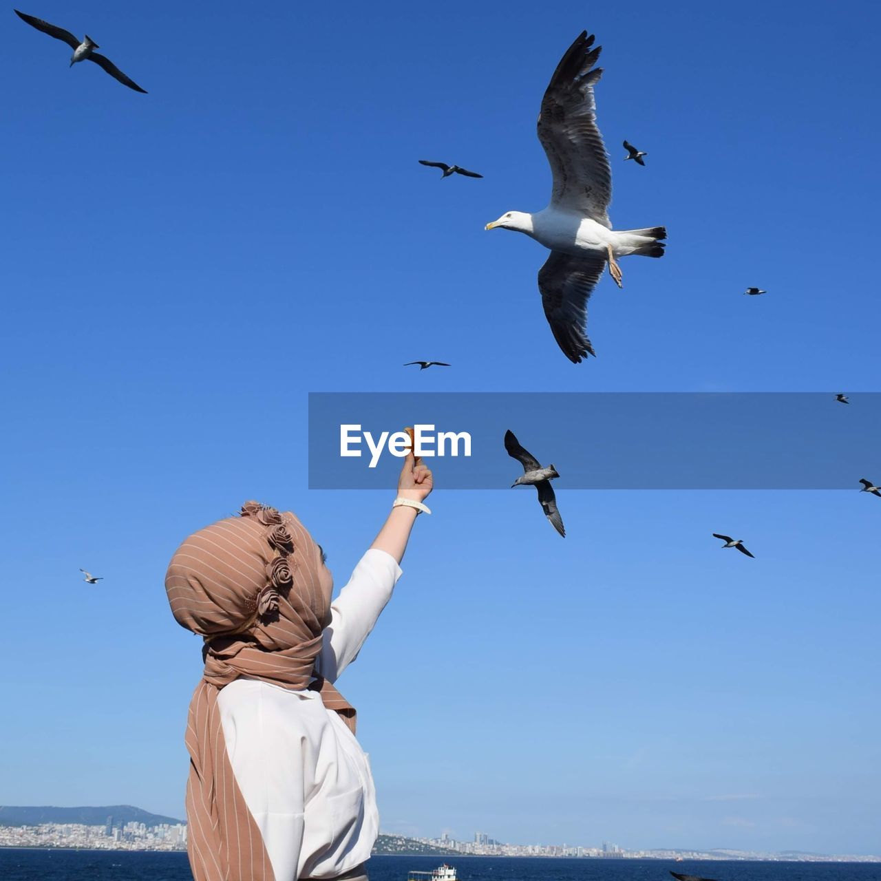 Young woman feeding birds against sky