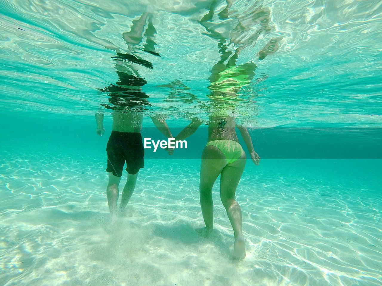 Low section of couple holding hands while swimming underwater