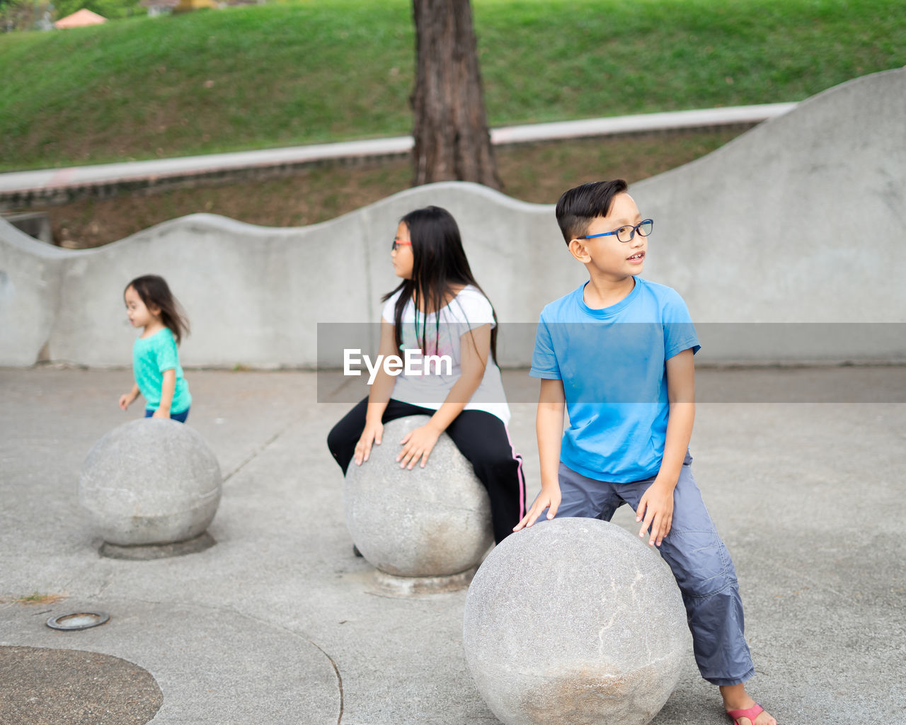 Asian children sitting on the concrete sphere ball shape in the park.