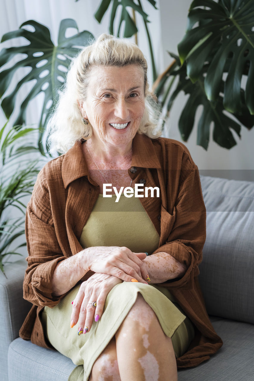 Cheerful elderly woman sitting on sofa at home