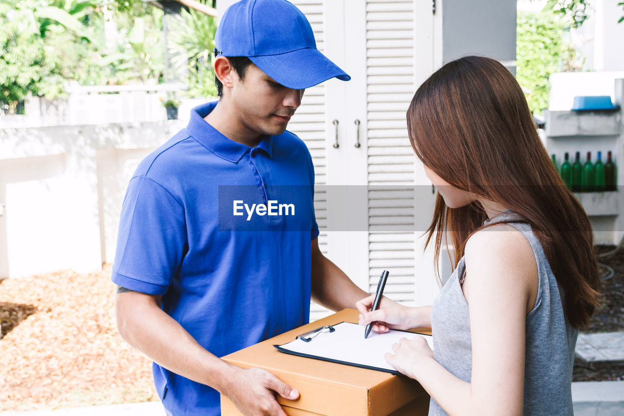 Woman signing on paper while salesman holding cardboard box