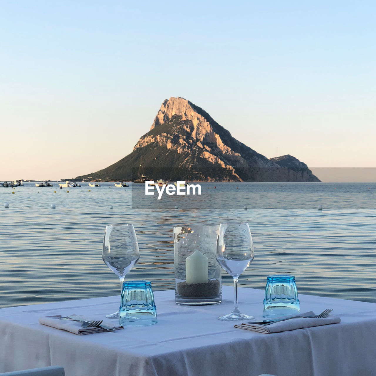 Lounge chairs and table at beach against clear sky dinner wine sunset