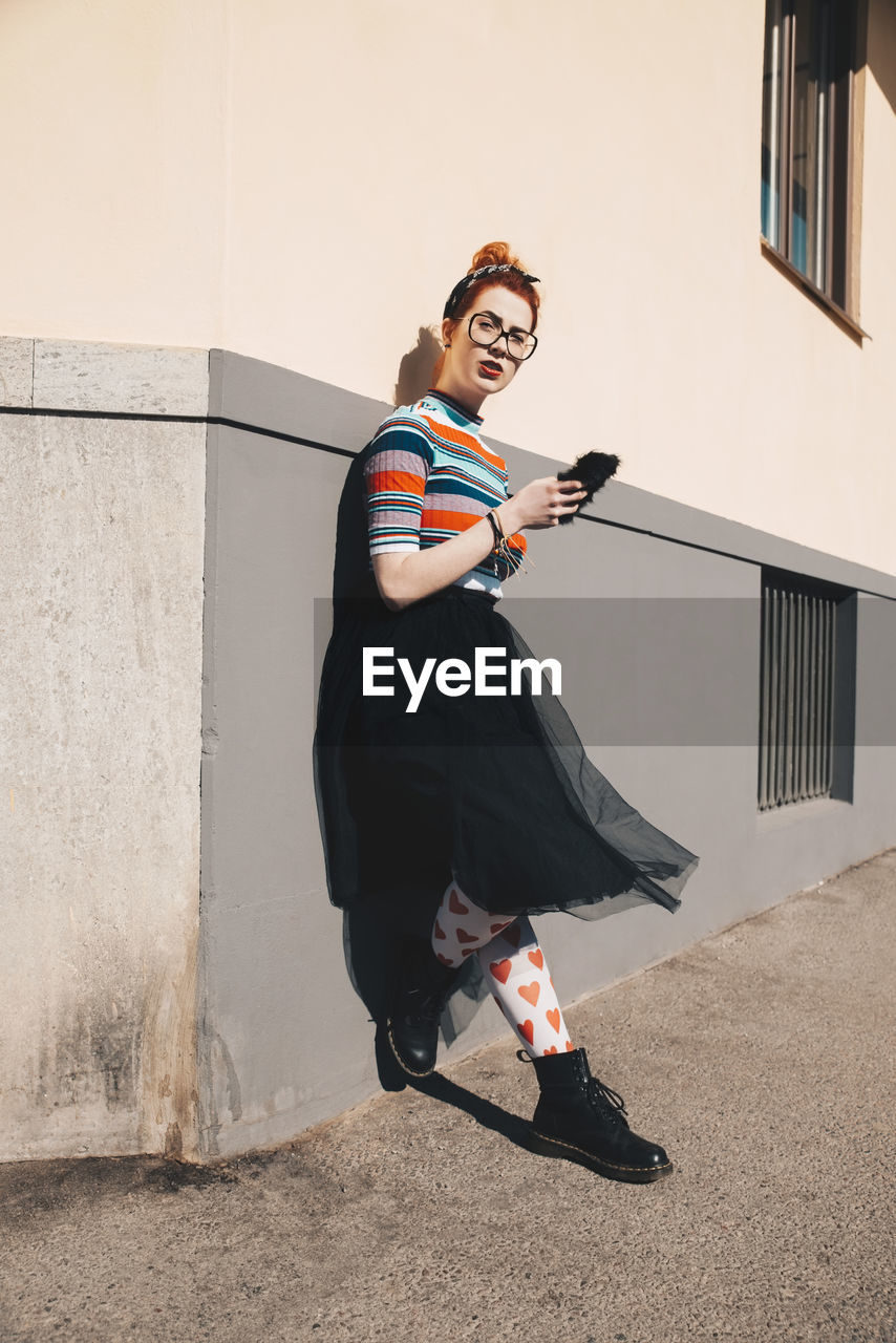 Full length of young woman using mobile phone while standing by wall