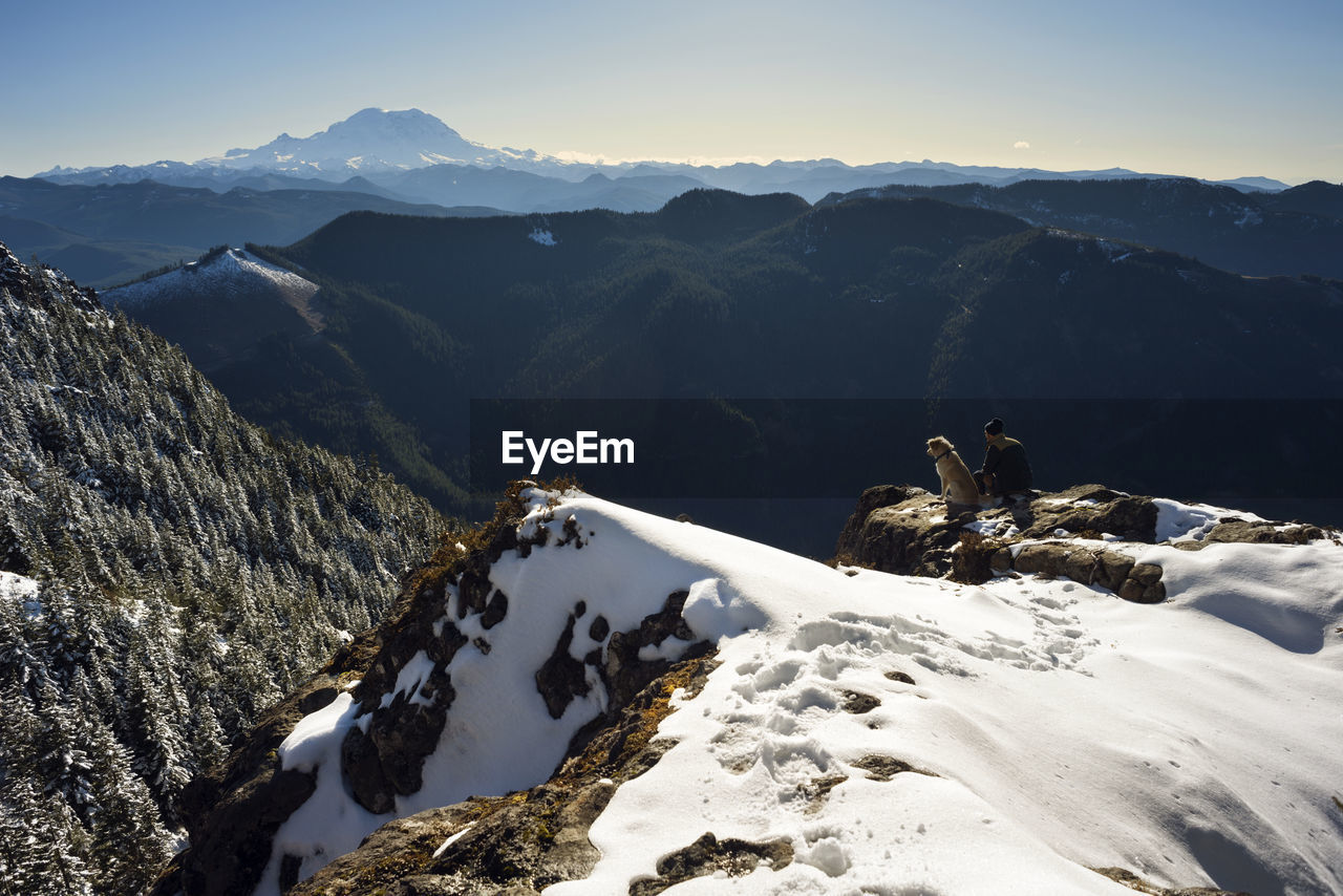 High angle view of man sitting with dog on snowcapped mountain