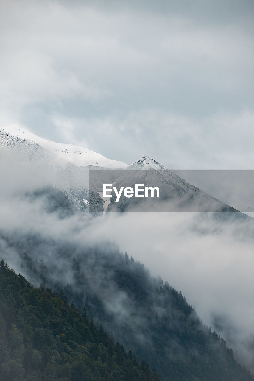 Scenic view of a mountain surrounded by clouds against sky