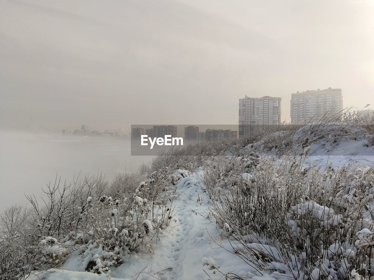 FROZEN RIVER AMIDST BUILDINGS AGAINST SKY