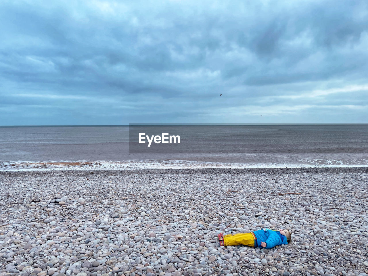 Scenic view of child laying on beach against sky