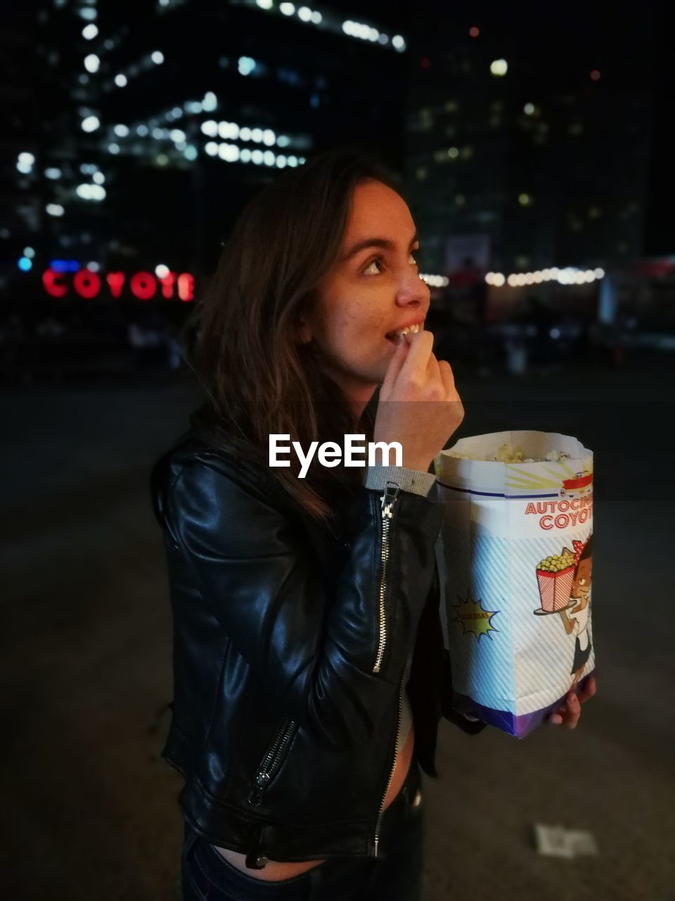 Young woman eating popcorn on street in city at night