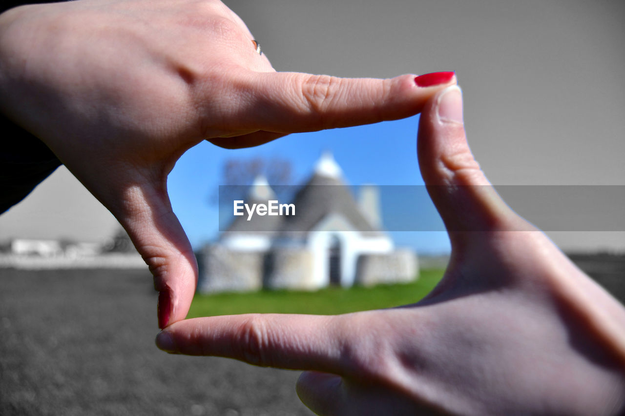 CLOSE-UP OF PERSON HOLDING HAND AGAINST BUILDING