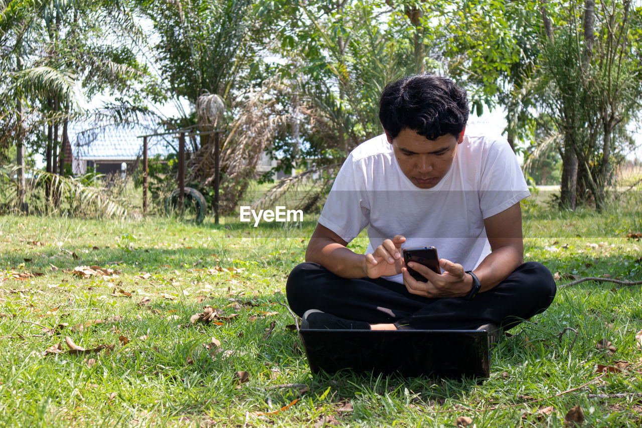 YOUNG MAN USING SMART PHONE IN GRASS