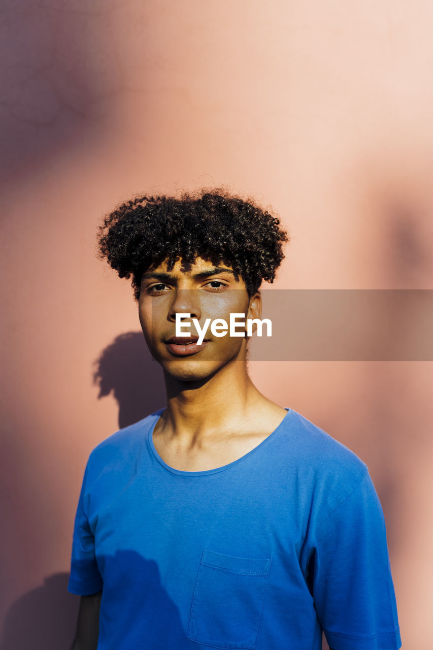 Young man with curly hair standing in front of coral wall