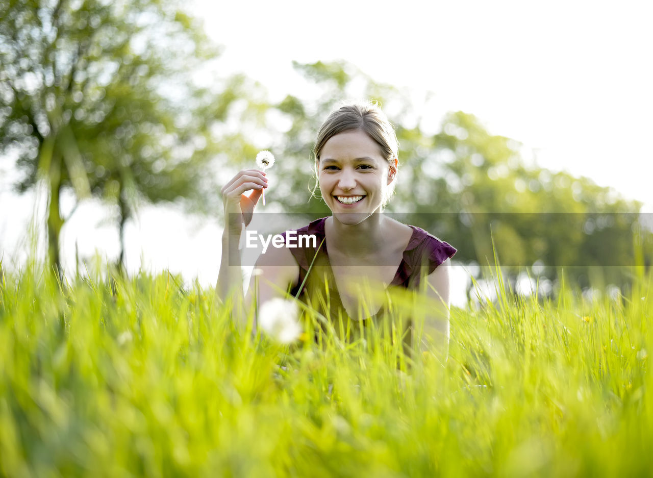 Portrait of smiling woman holding dandelion on grassy field