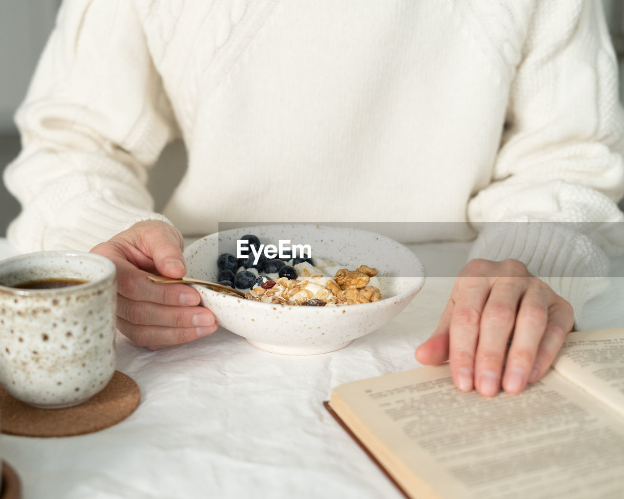 Reading book and eating healthy holiday winter breakfast with granola muesli and yogurt in bowl 