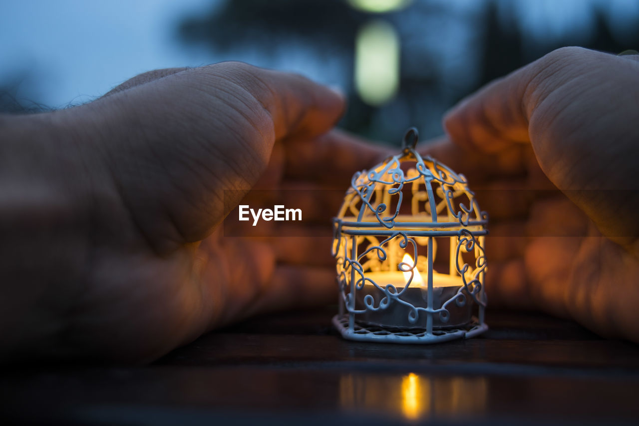 Cropped hands by candle on table at dusk