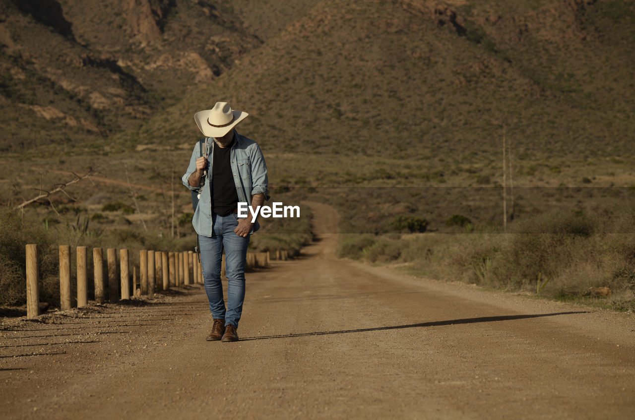 Adult man in cowboy hat walking on dirt road