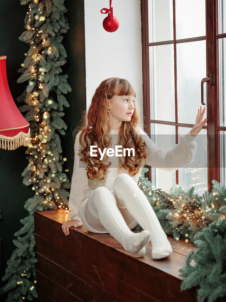 Happy young girl sitting by the window and christmas tree