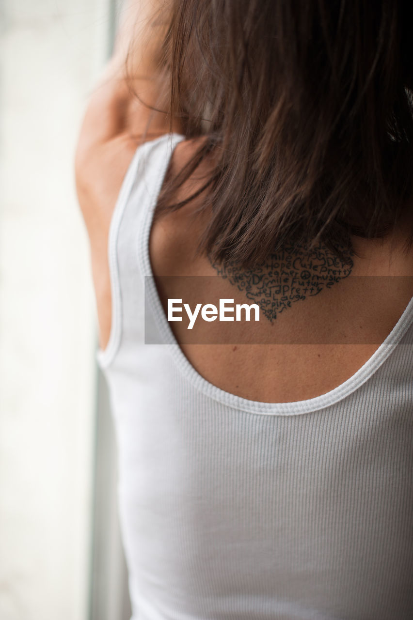 Rear view of woman with tattoo standing at home