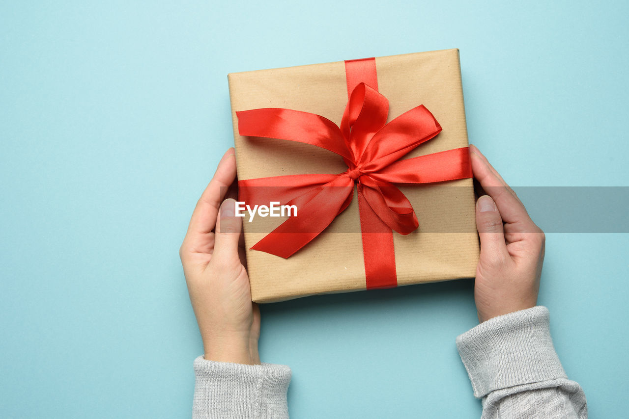 Cropped hand of woman holding gift box over blue background