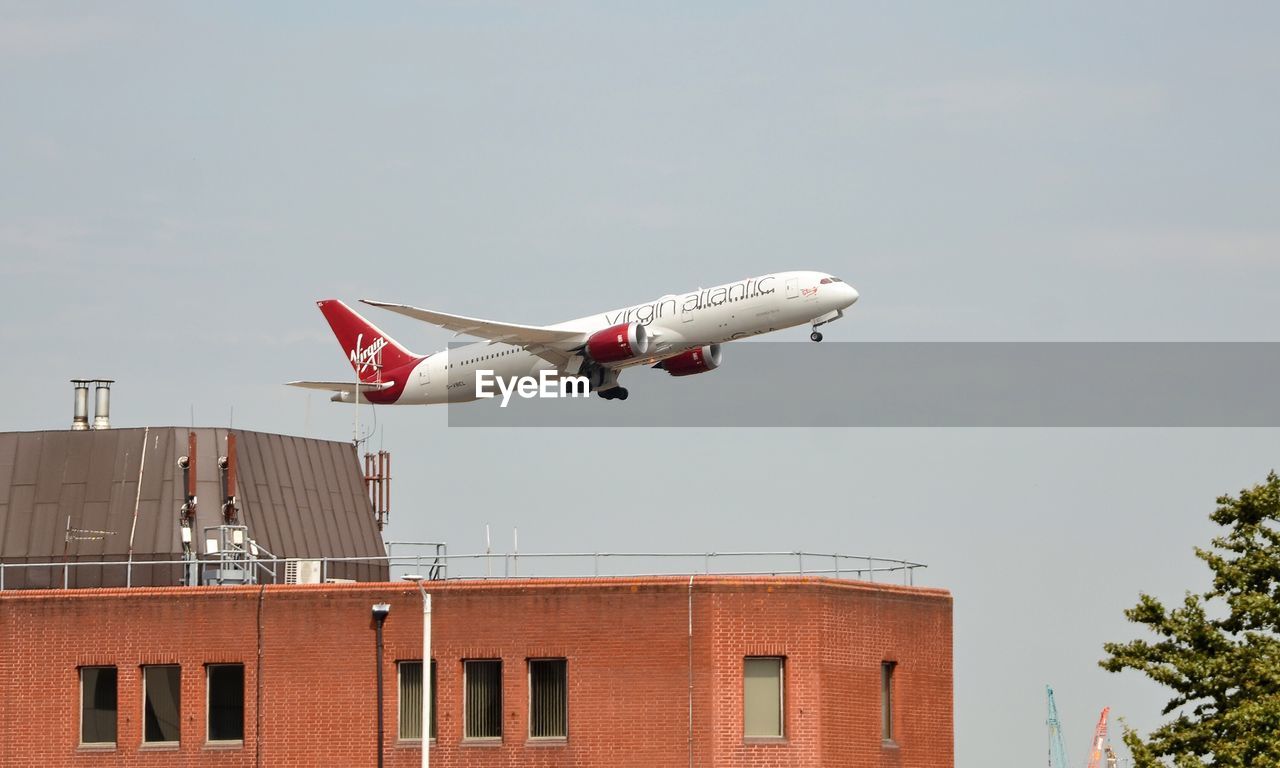 LOW ANGLE VIEW OF AIRPLANE FLYING AGAINST BUILDING