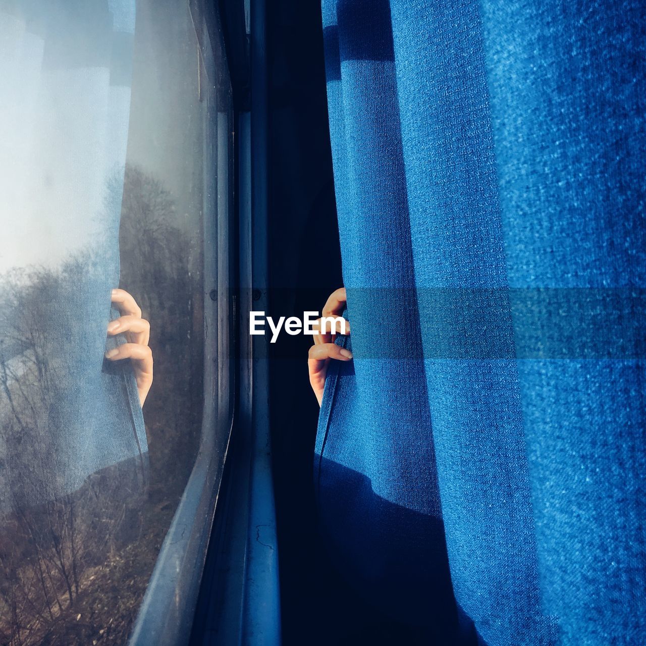 Close-up of hand holding curtain against window