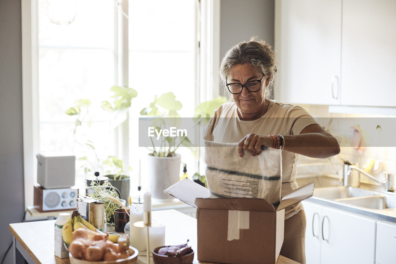 Mature woman with disability opening package in kitchen at home