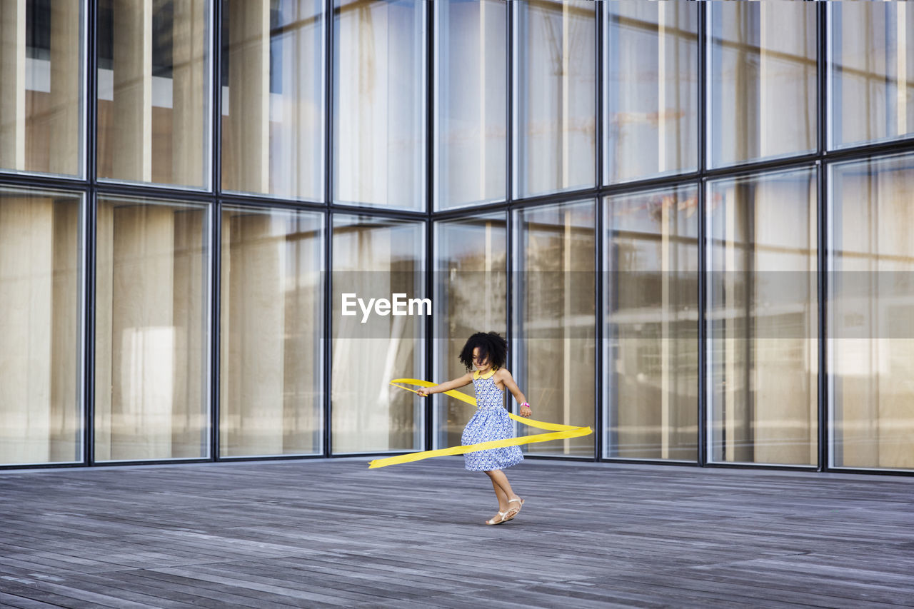 Full length of girl playing with ribbon against modern building