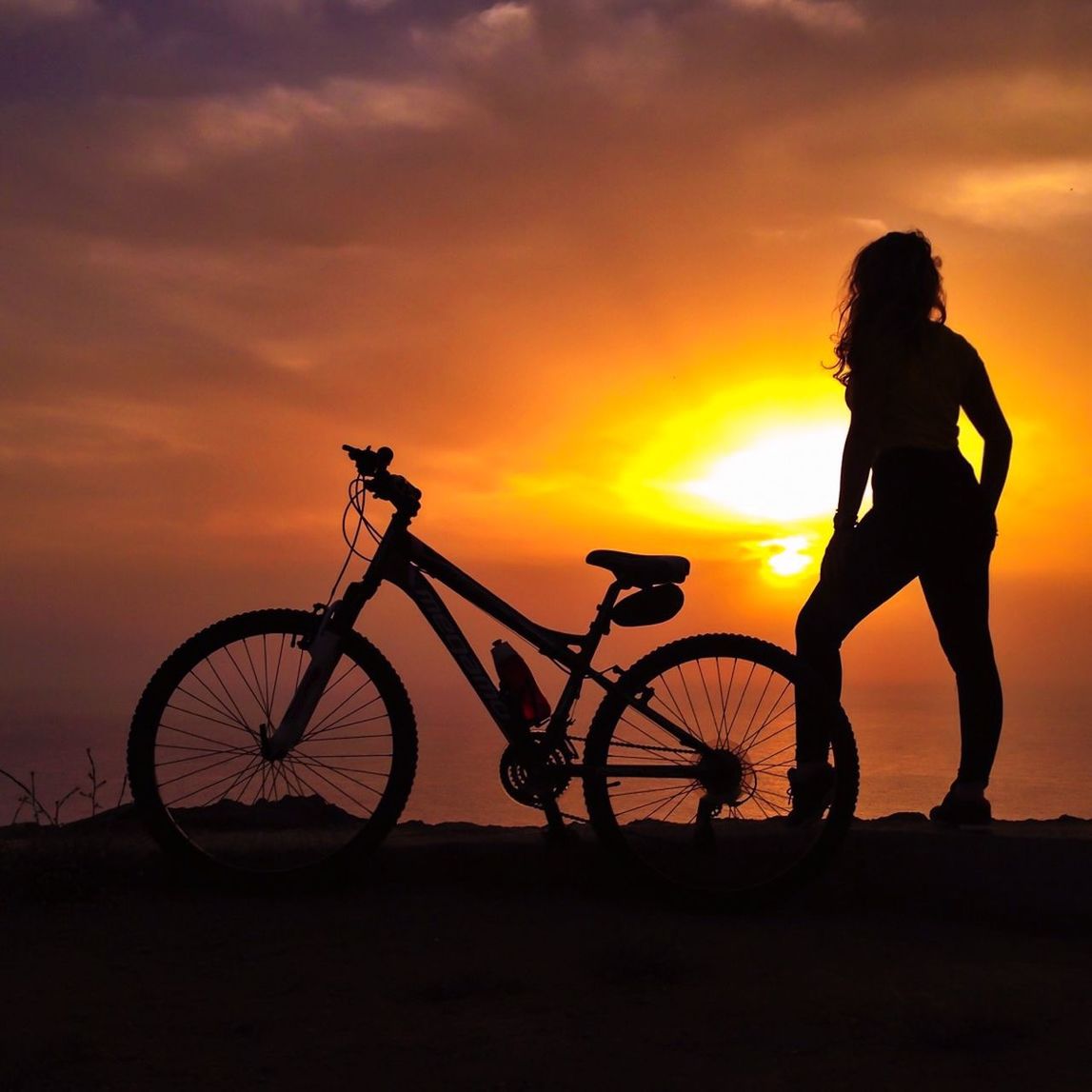 Silhouette woman with bicycle standing against sky during sunset