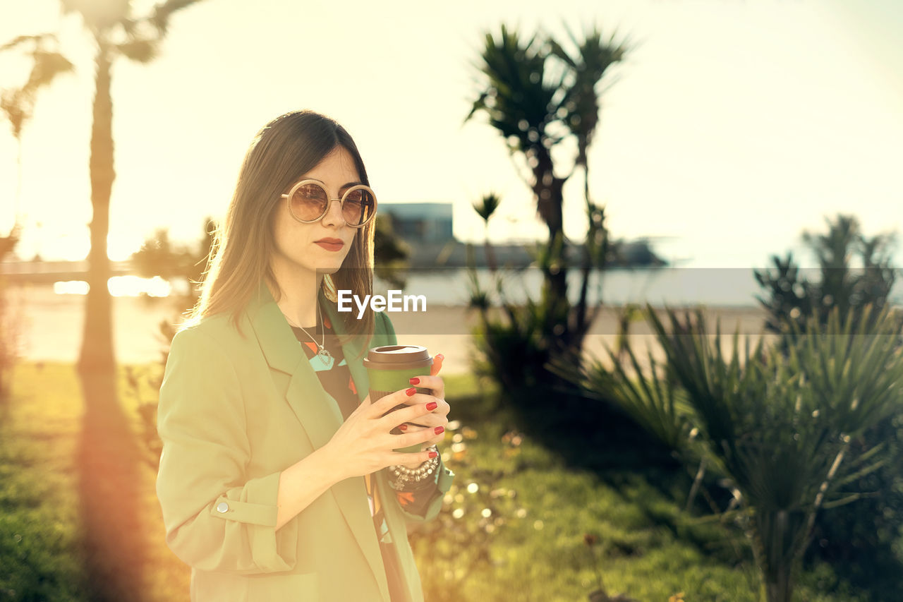 Woman with coffee cup standing in park