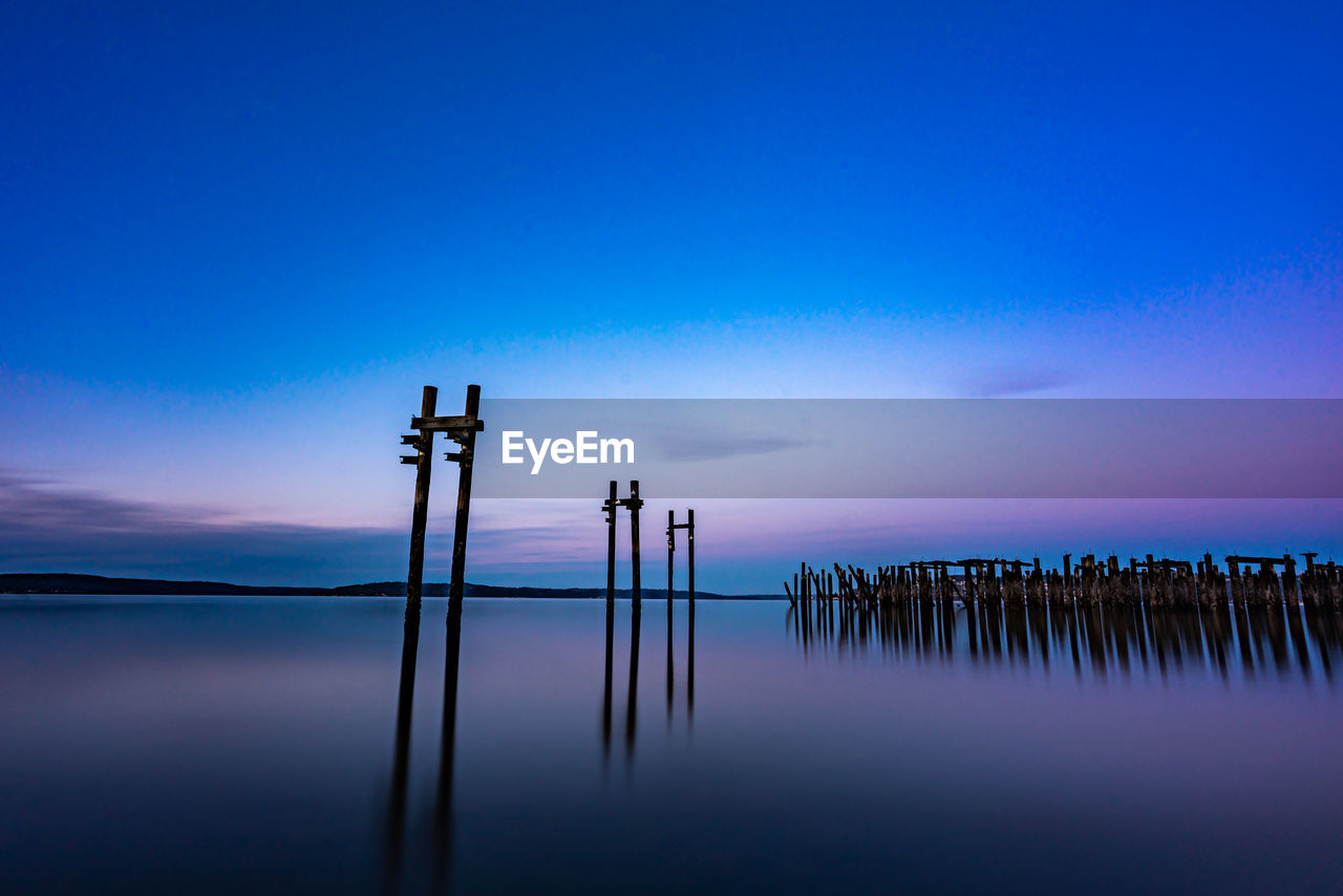 Wooden posts in water against sky at sunset