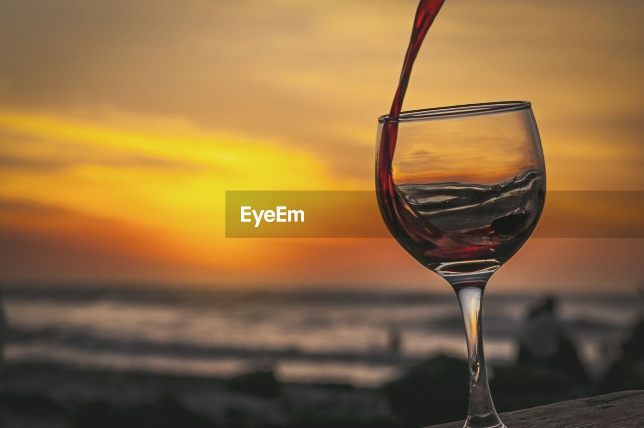CLOSE-UP OF WINEGLASS ON BEACH AGAINST SUNSET