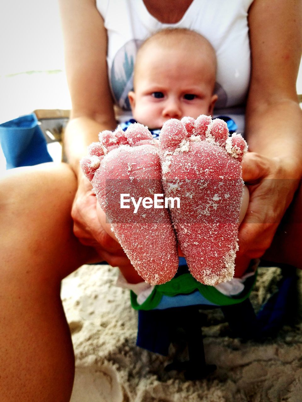 Midsection of mother holding baby boy with sandy feet at beach